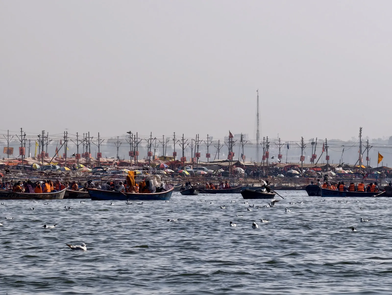 Boats on the Ganga below the flags and poles of the Mela