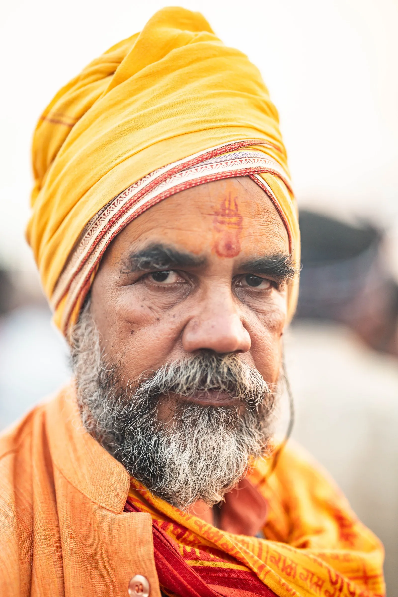 An elderly sadhu in a yellow turban and saffron shawl at the Kumbh Mela, Prayagraj
