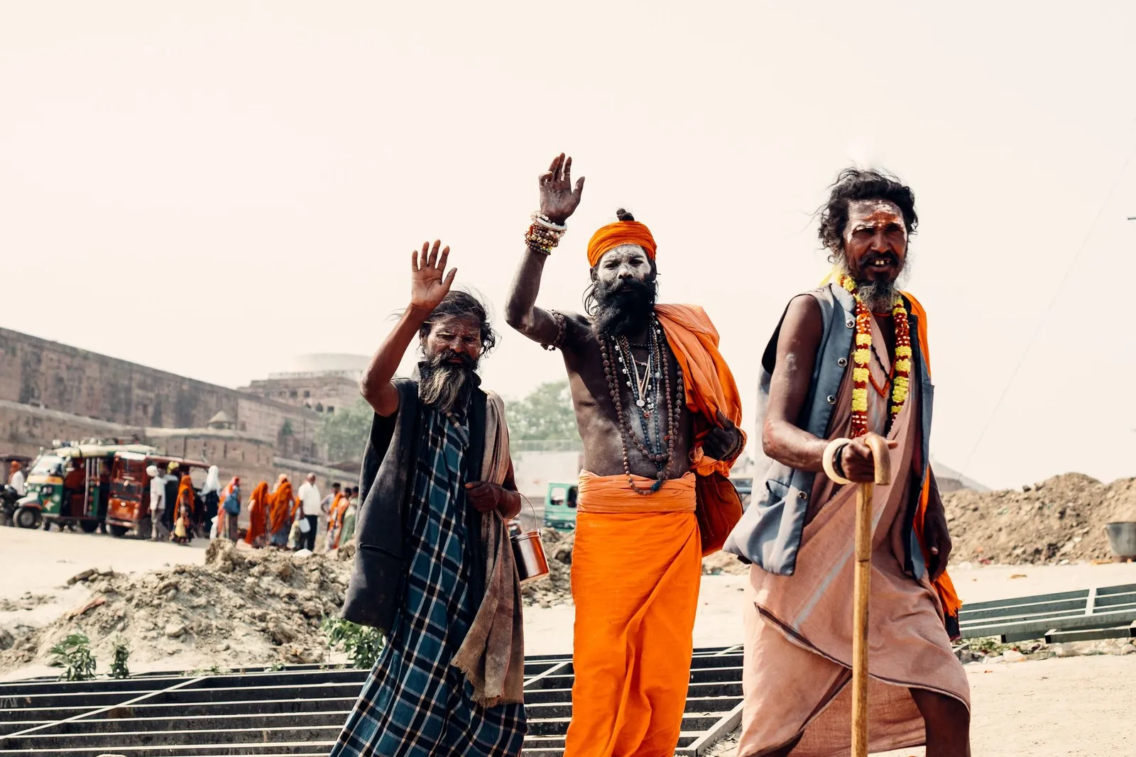 Three sadhus, arms raised in greeting, walking by the river at Prayagraj