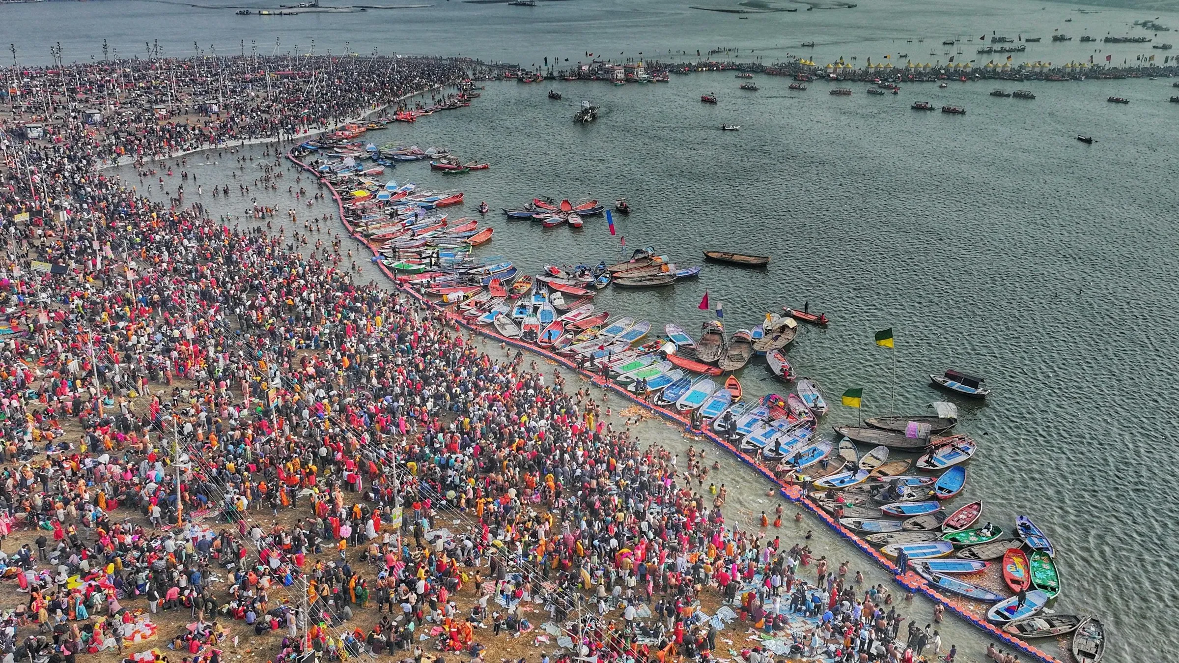 Pilgrims crowding the sandbank at the Triveni Sangam, with rowing boats massed along the water, Prayagraj