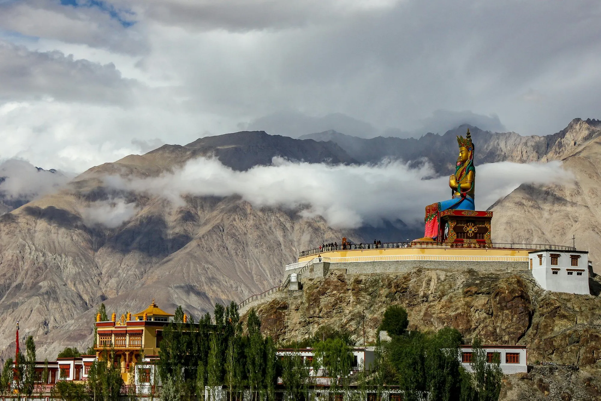 A giant Buddha statue on a ridge above a monastery