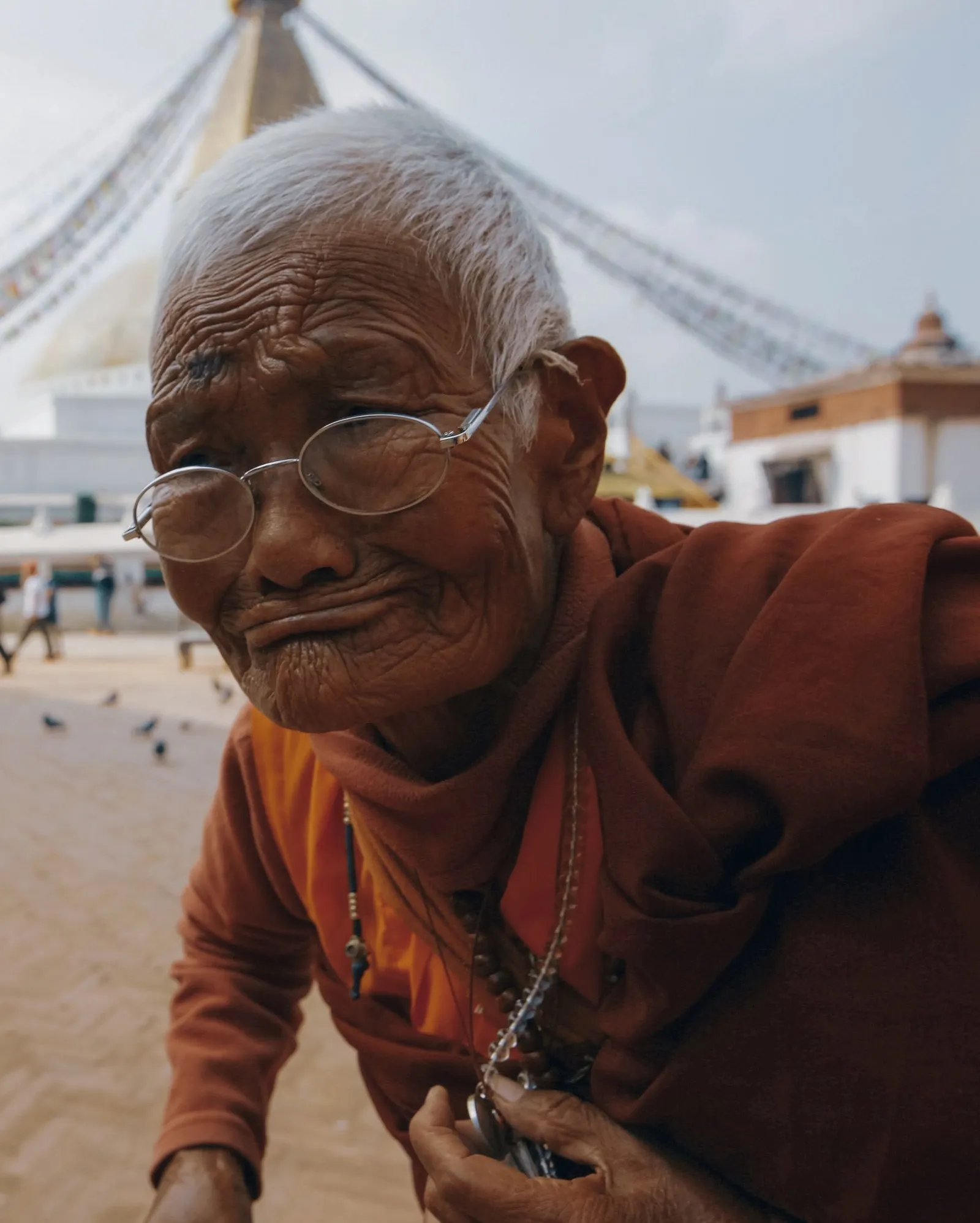 An elder in maroon robes with prayer beads at the Boudhanath stupa, Kathmandu