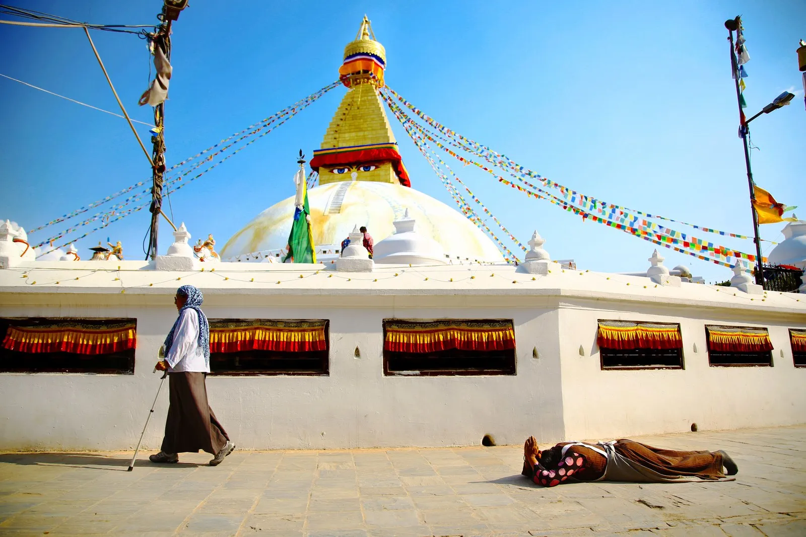Pilgrims on the kora round the Boudhanath stupa, one prostrating full length, Kathmandu