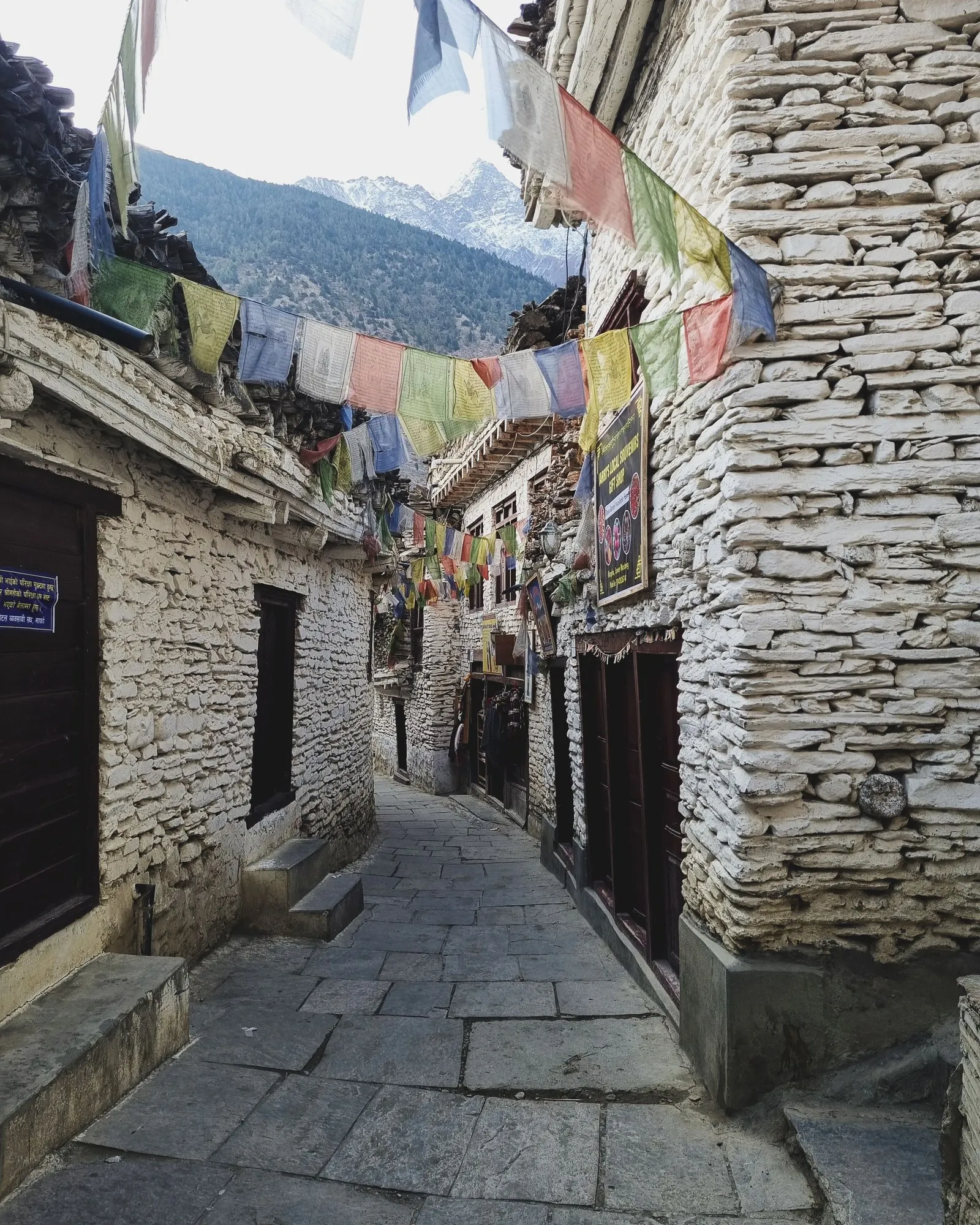 A flagstone lane between whitewashed stone houses under prayer flags, Mustang