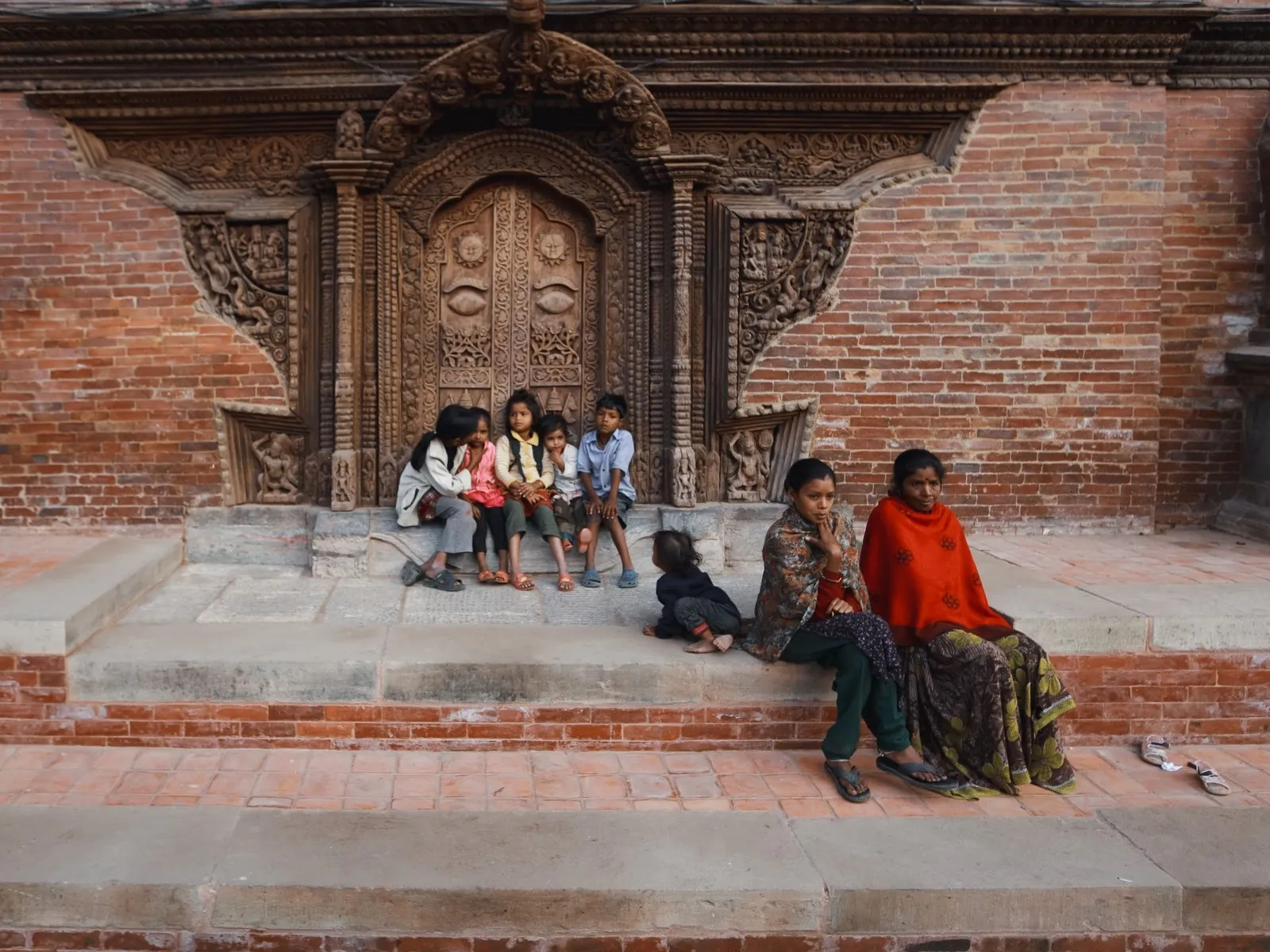 A woman and children on the steps by a carved palace door in Patan Durbar Square