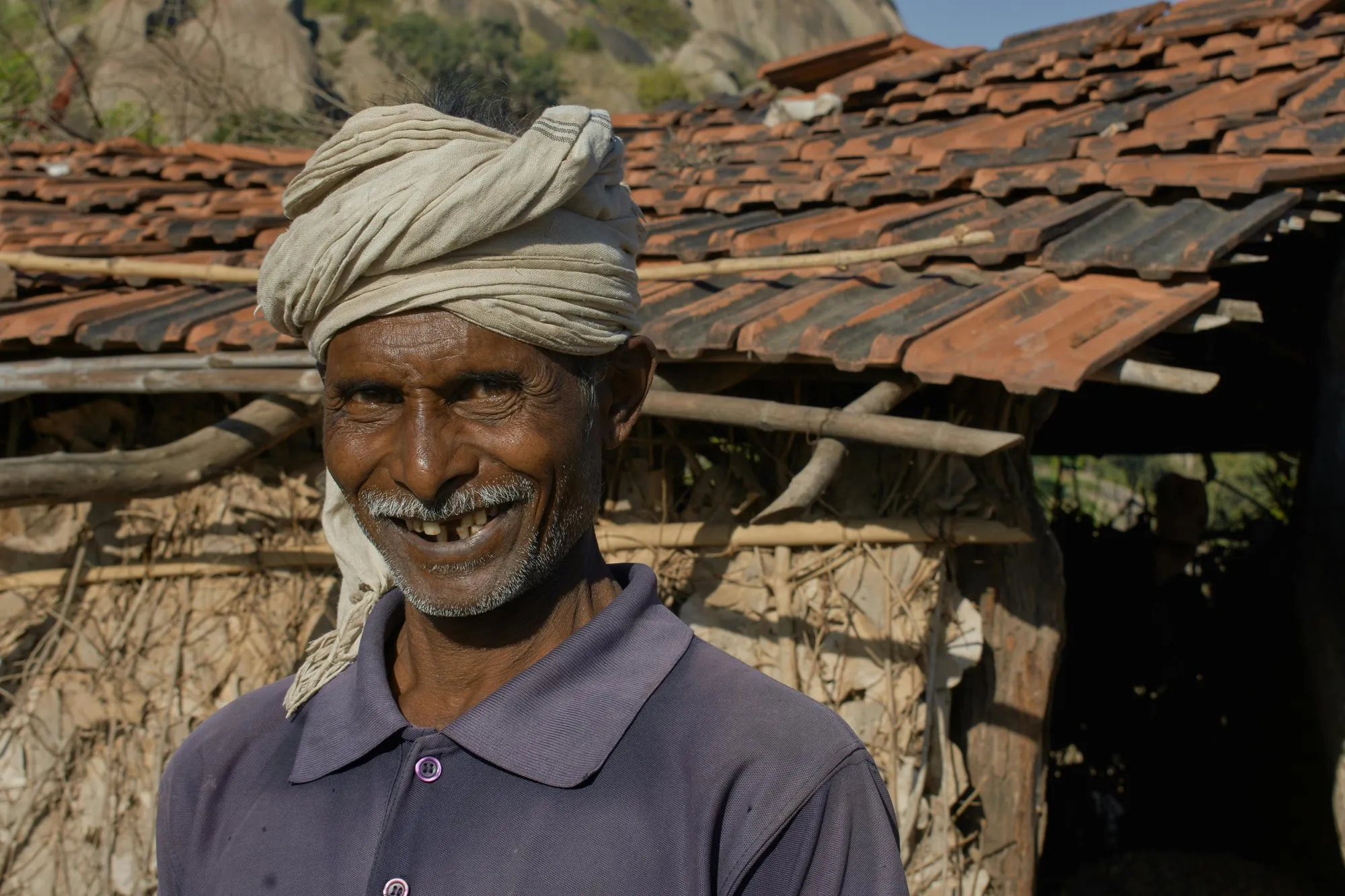 A man in a white turban smiling beside a tiled roof