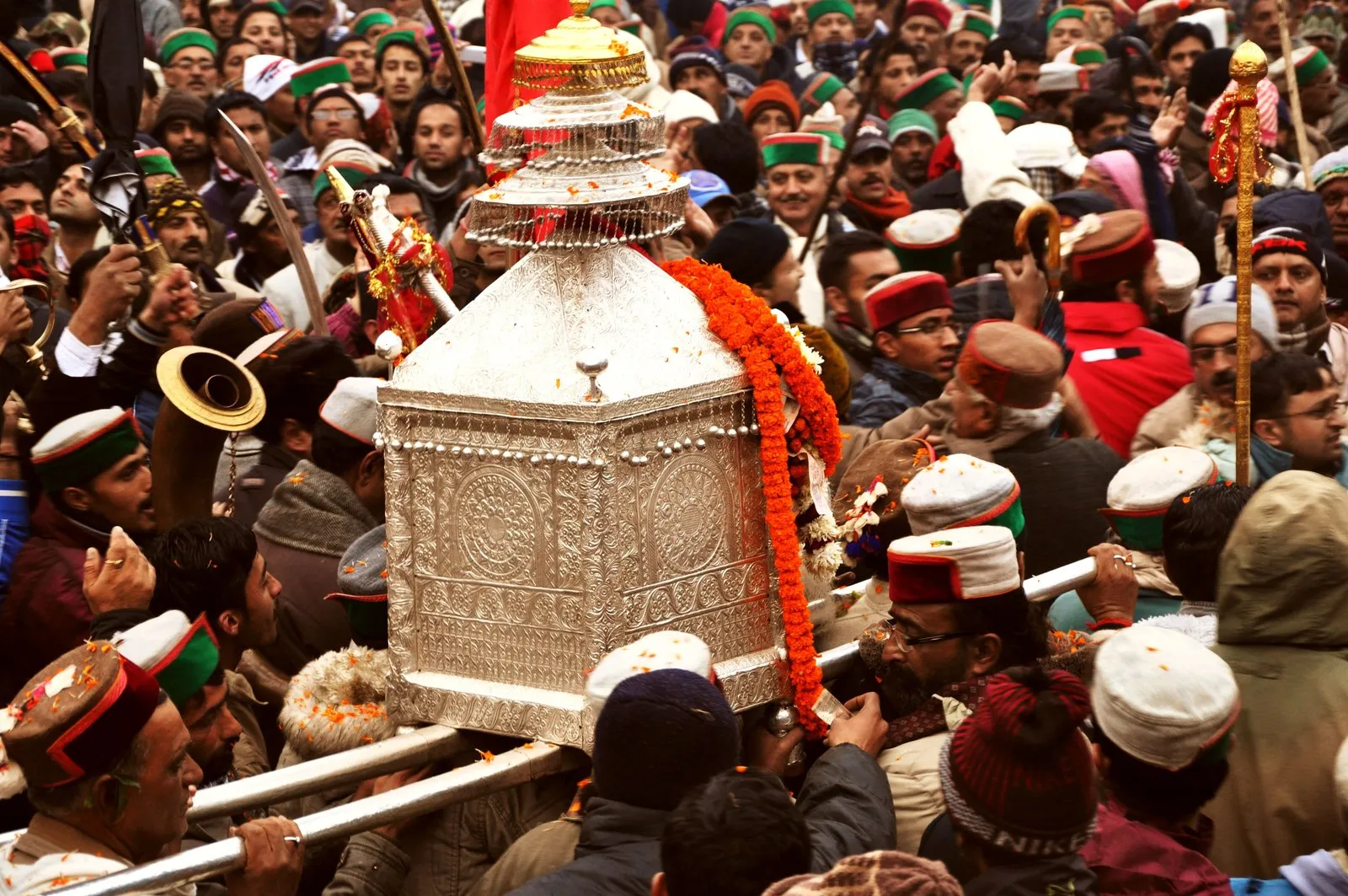 A village deity carried through a crowd in Himachali caps, Shimla district