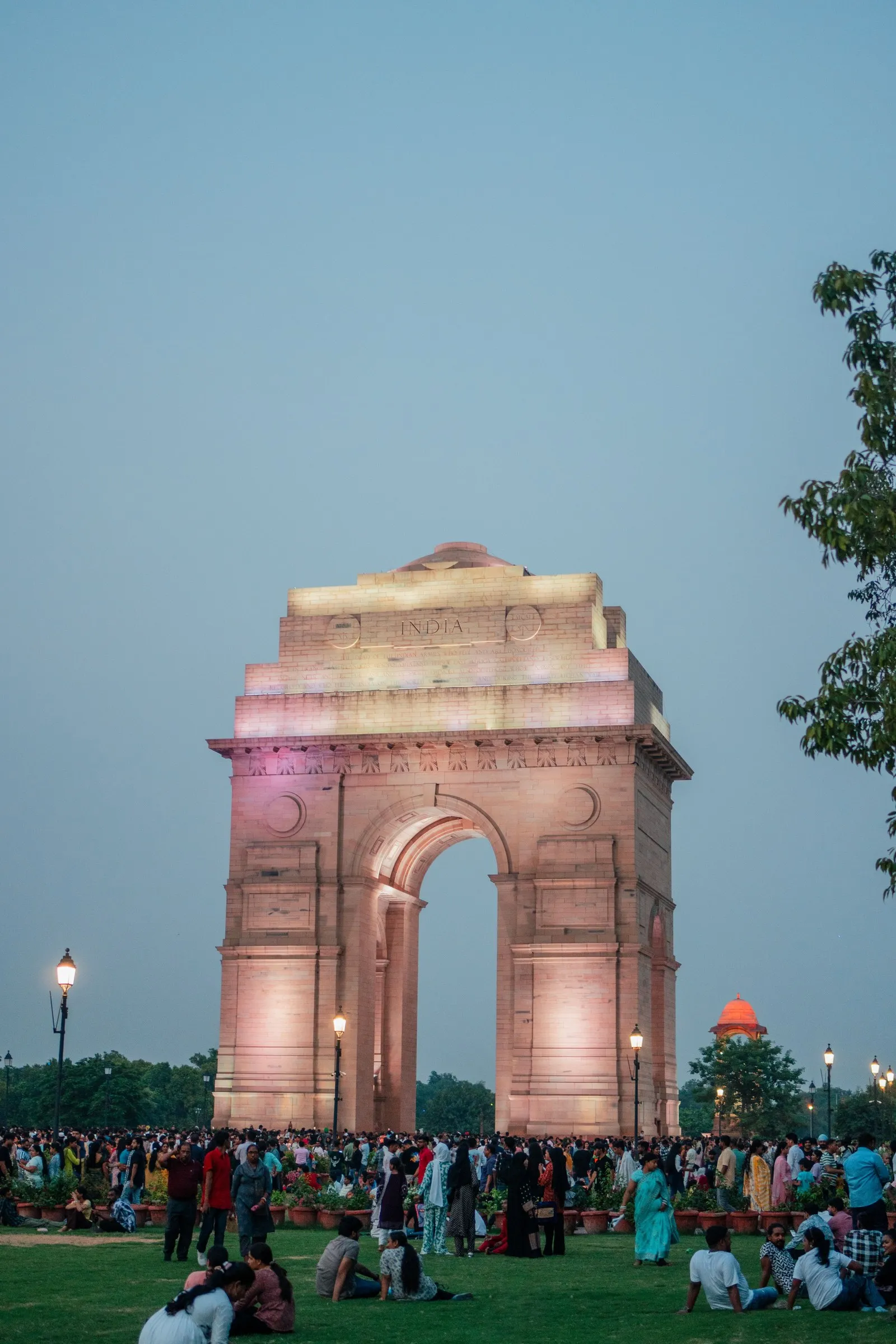 India Gate lit at dusk, the evening crowd on the lawns below it, New Delhi
