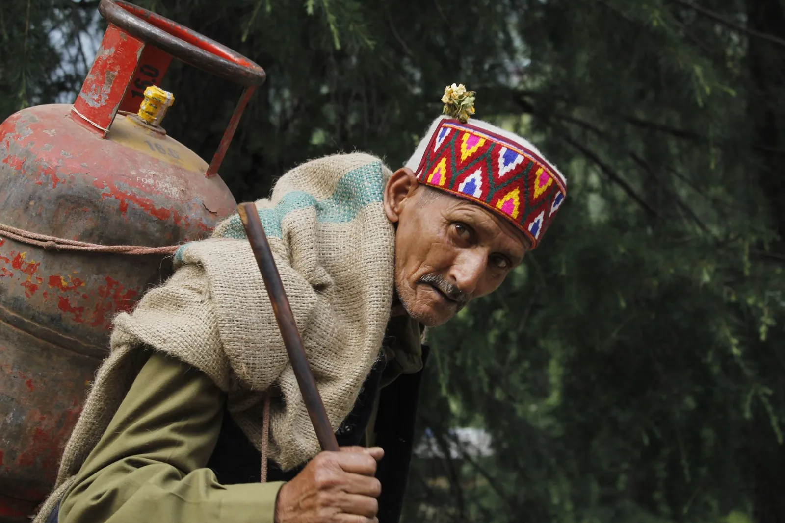 A man in a Kullu cap carrying a gas cylinder on his back, Manali