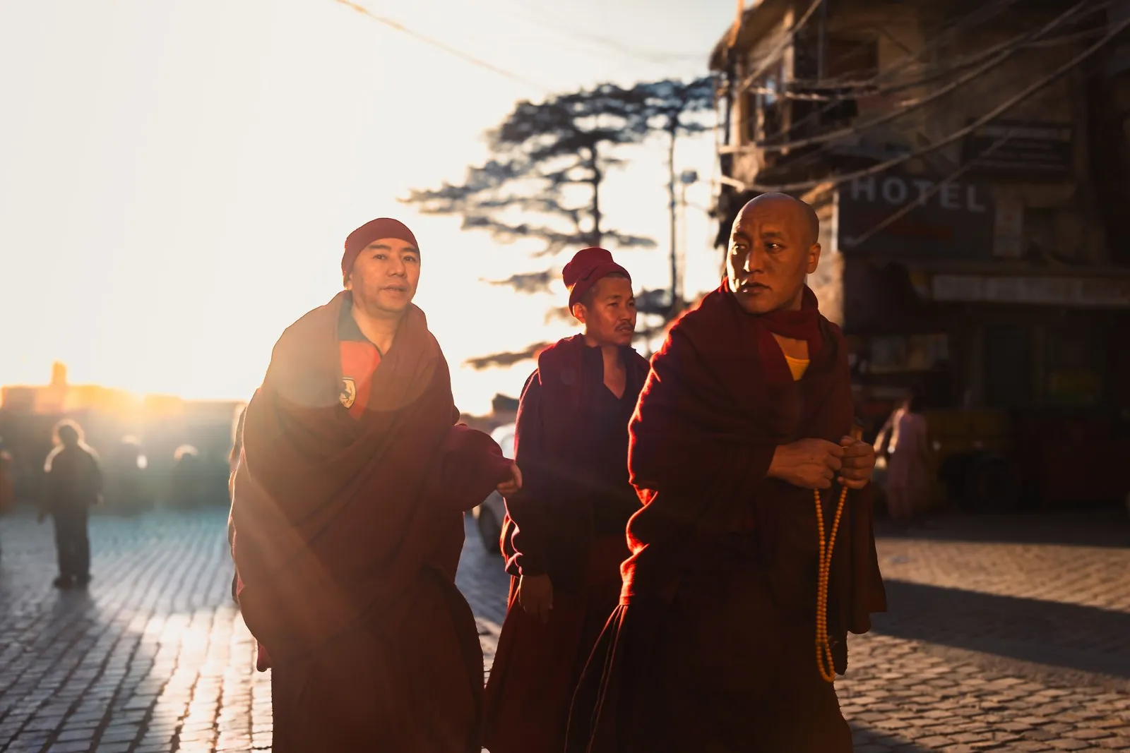 Three monks in maroon robes walking in the early sun, Dharamshala