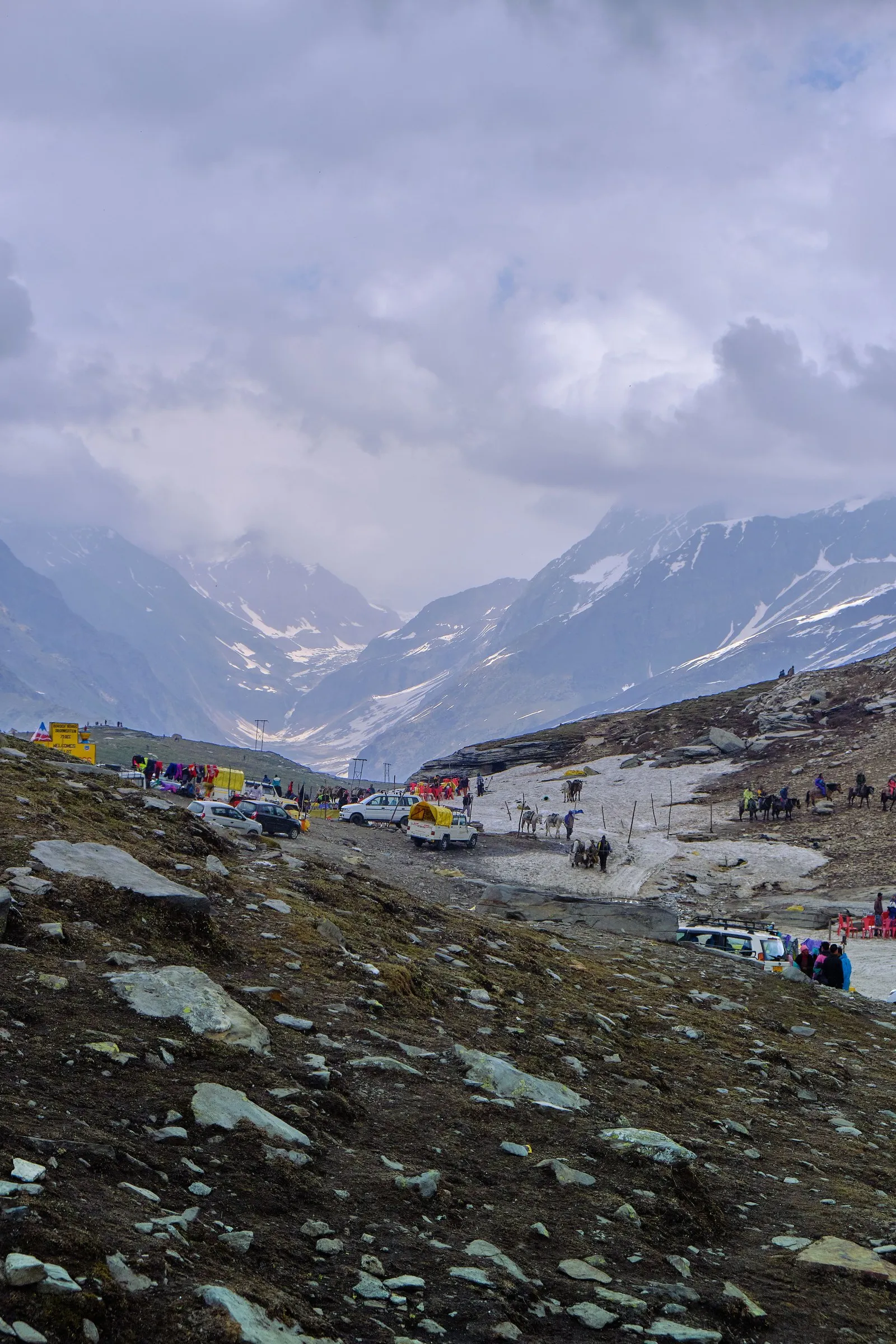 Travellers and parked cars on the snow at Rohtang Pass, the mountains beyond
