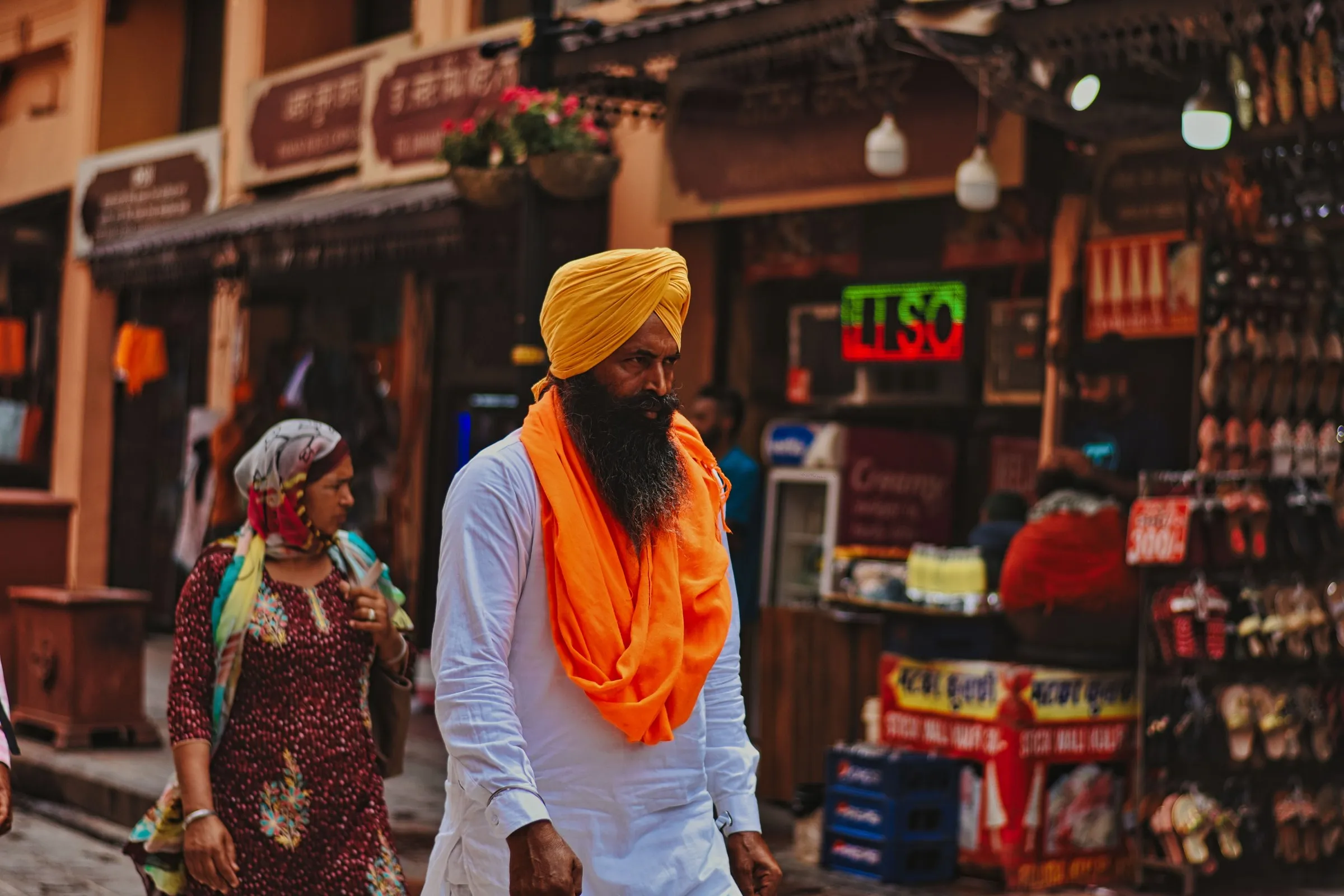 A Sikh man in a saffron turban and scarf walking through a bazaar in Amritsar