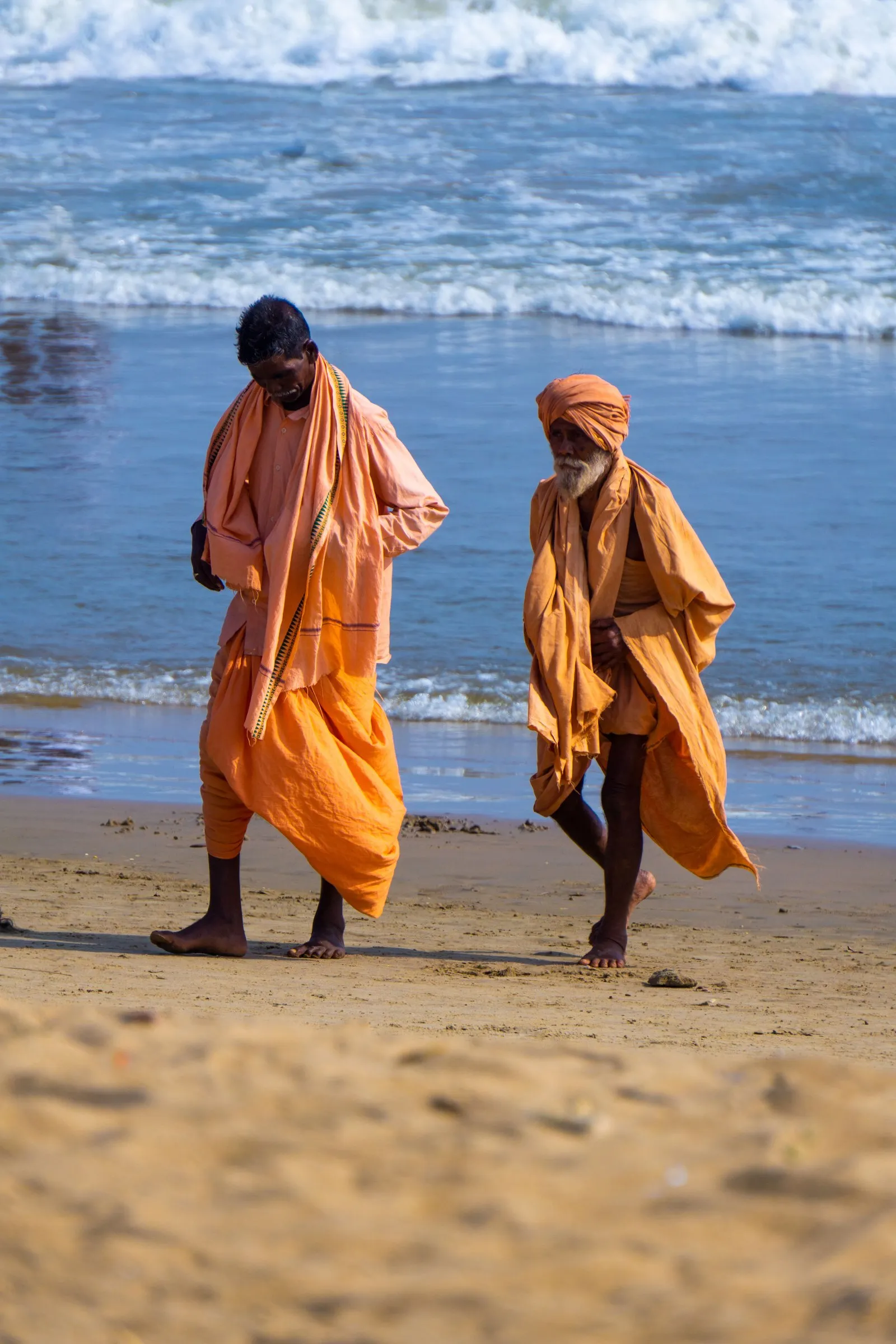 Two sadhus in saffron walking on the beach at Puri