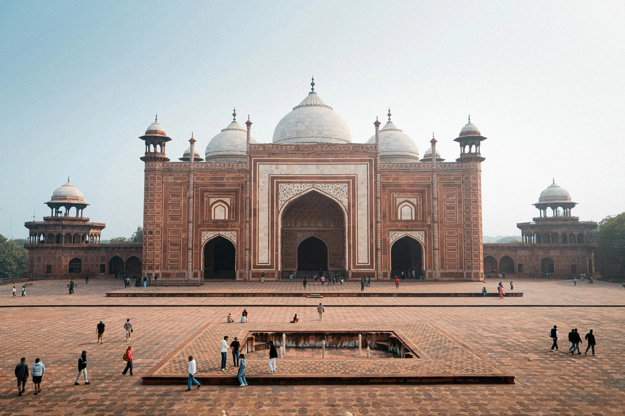 A red sandstone mosque with white domes in the Taj Mahal complex