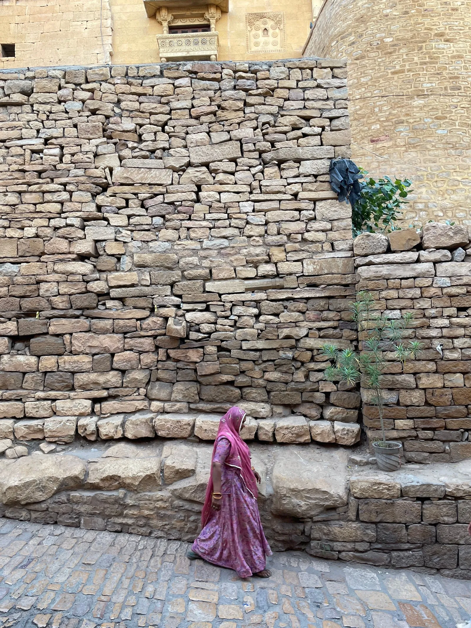 A woman in a pink sari walking along a stone lane in Jaisalmer