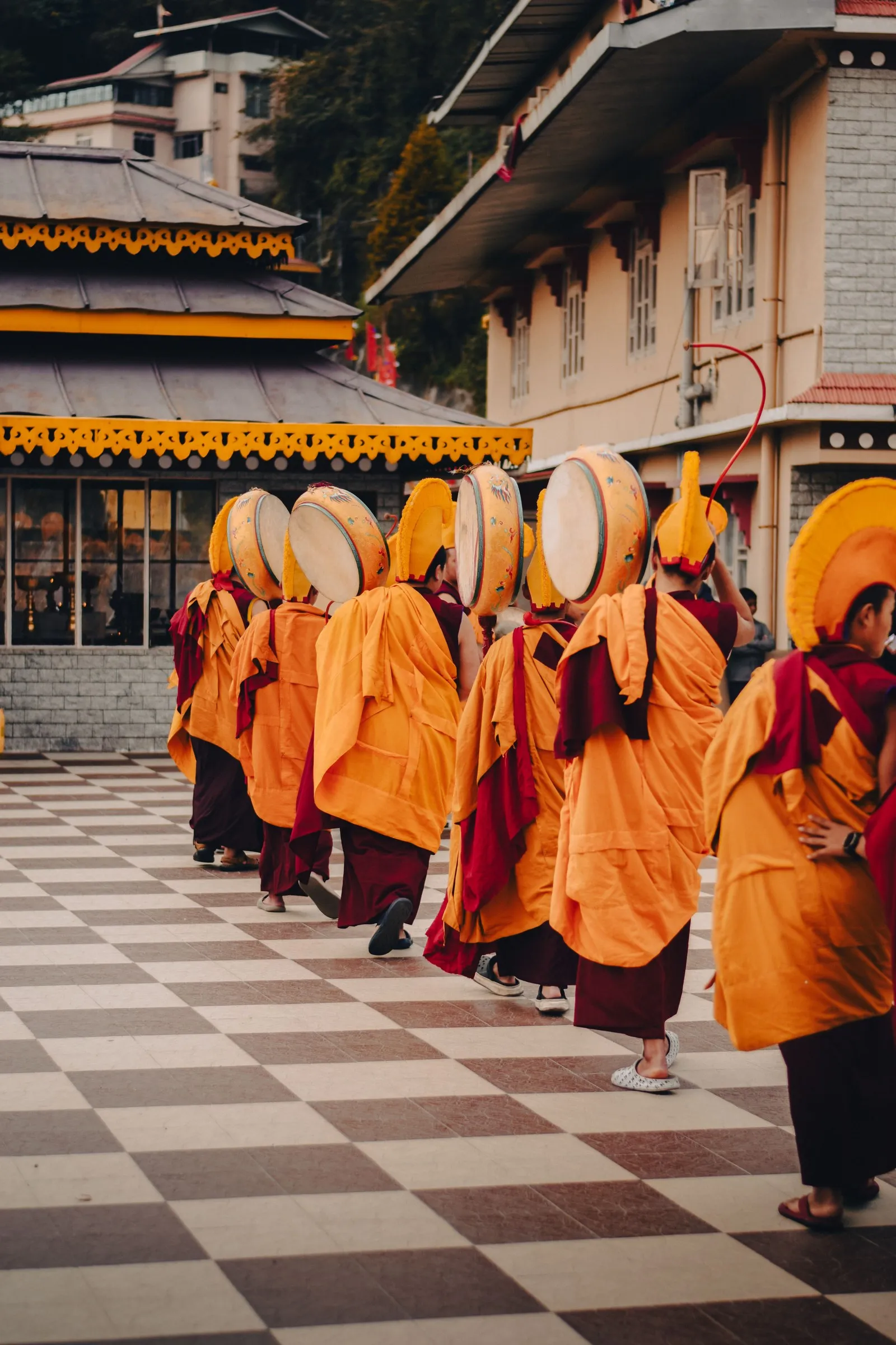 Monks in crested yellow hats carrying drums in procession at a monastery in Gangtok