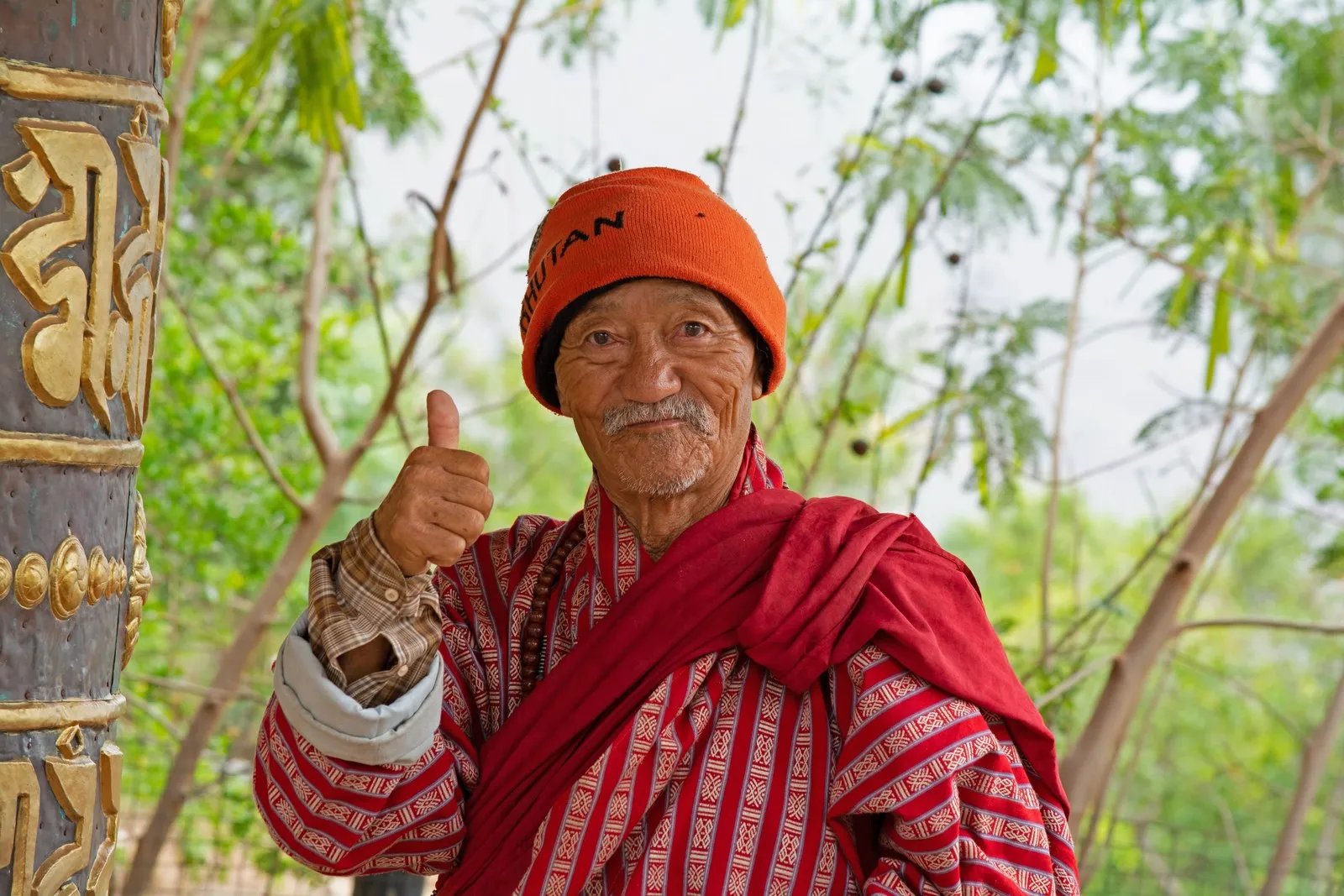 An elder in a red gho and orange cap in Thimphu, smiling