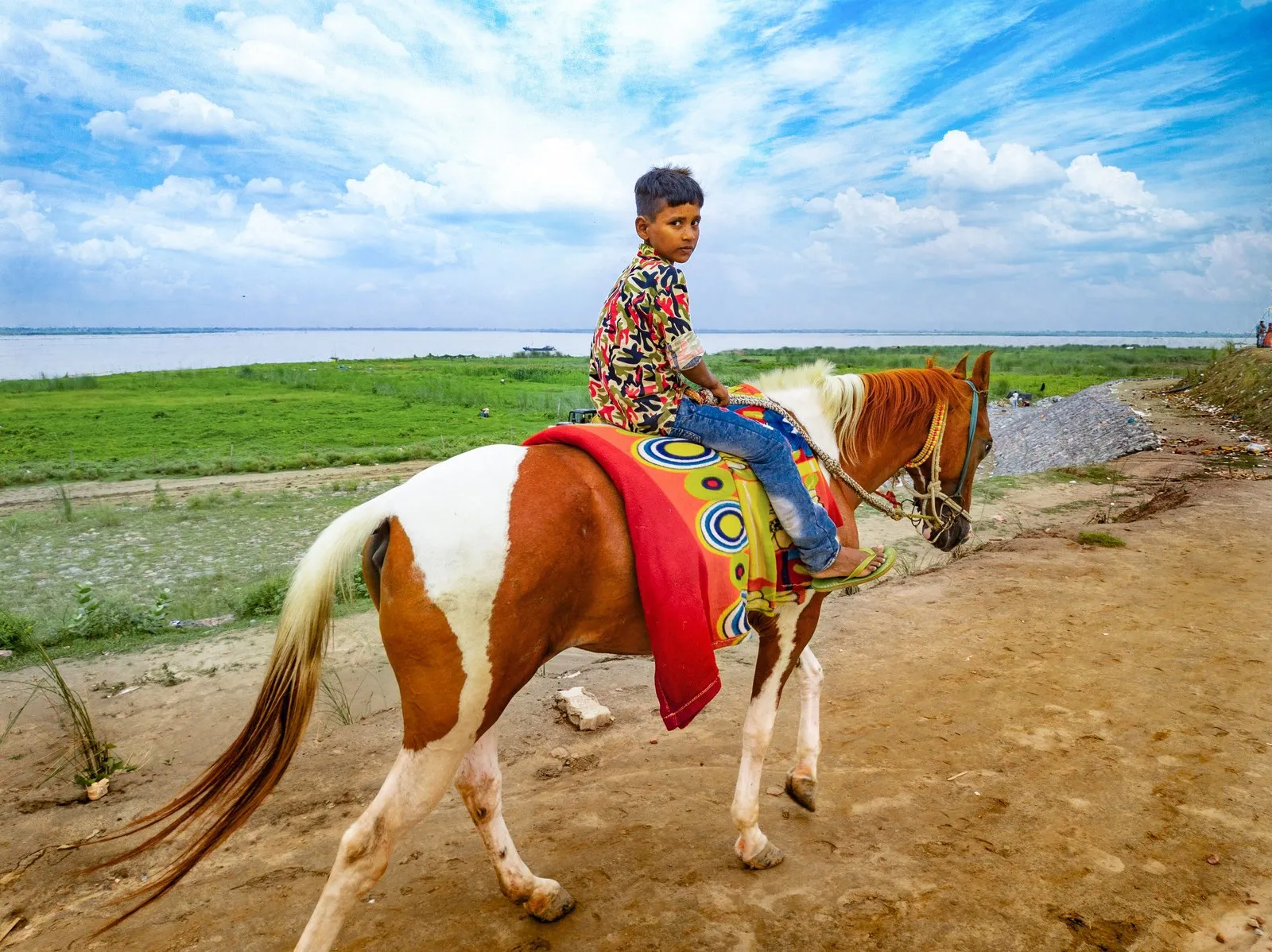 A boy riding a pony along a riverside track in rural Patna