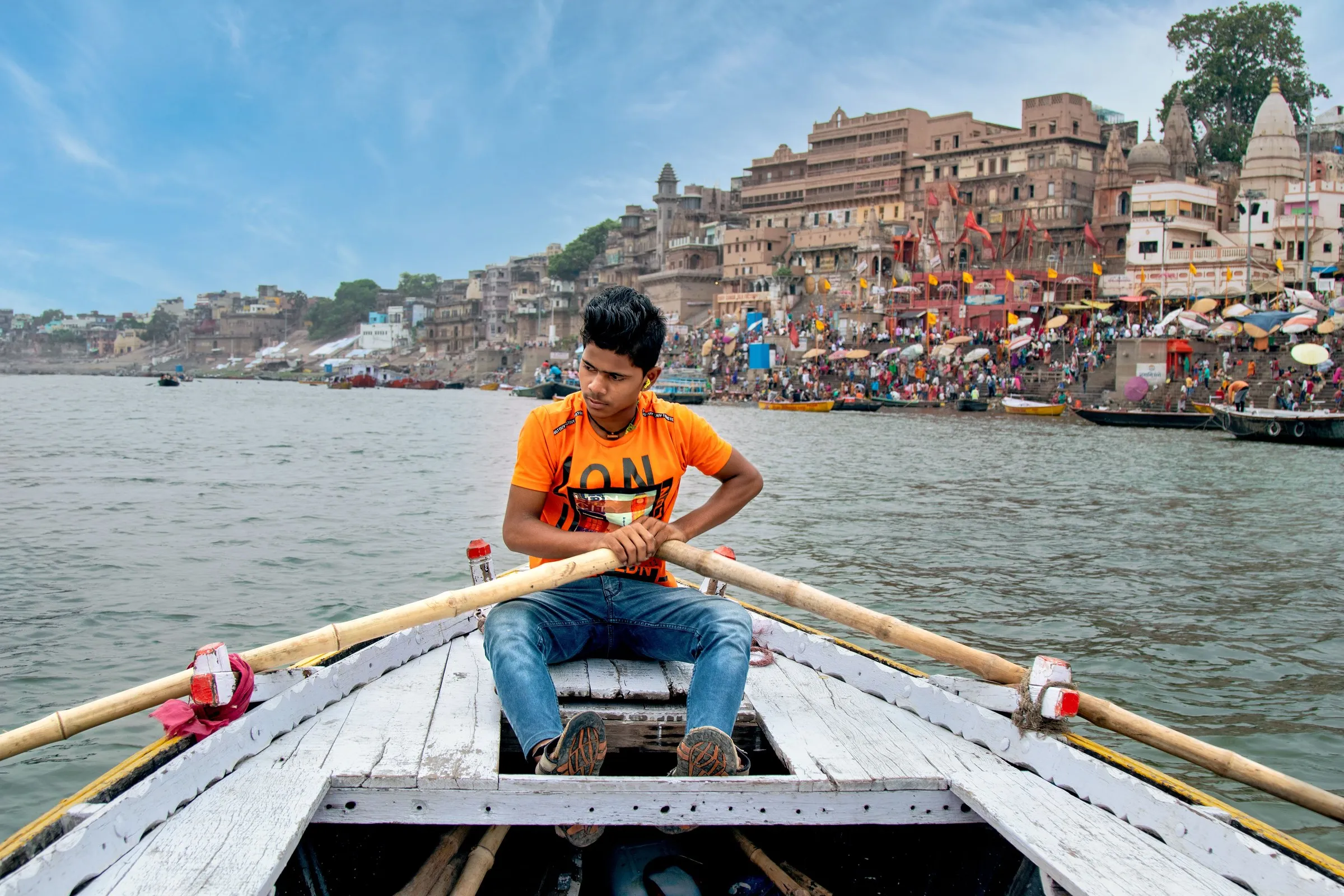 A young boatman rowing on the Ganga at Varanasi, the ghats behind him