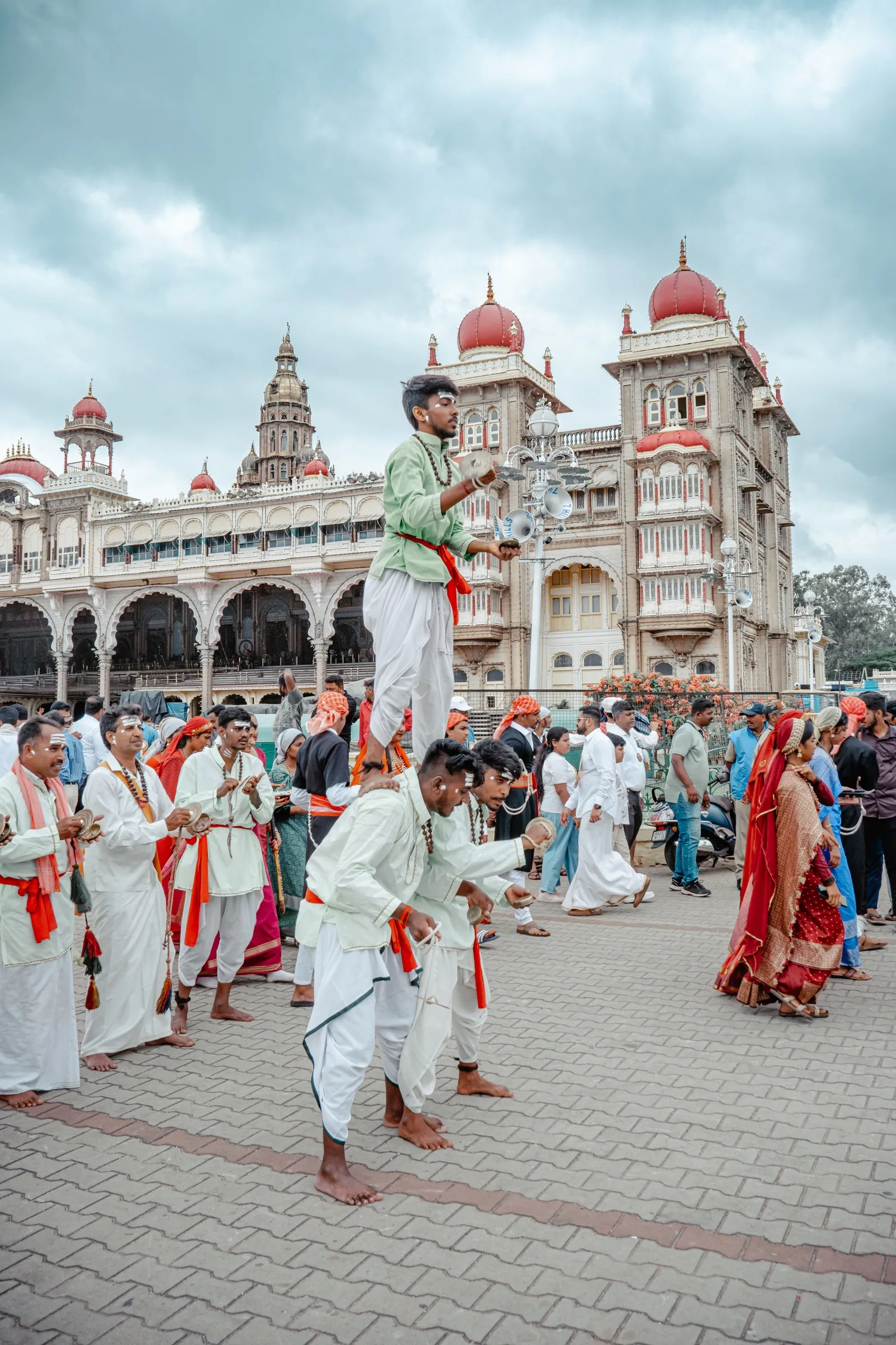 Performers in white and saffron in the forecourt of the Mysore Palace