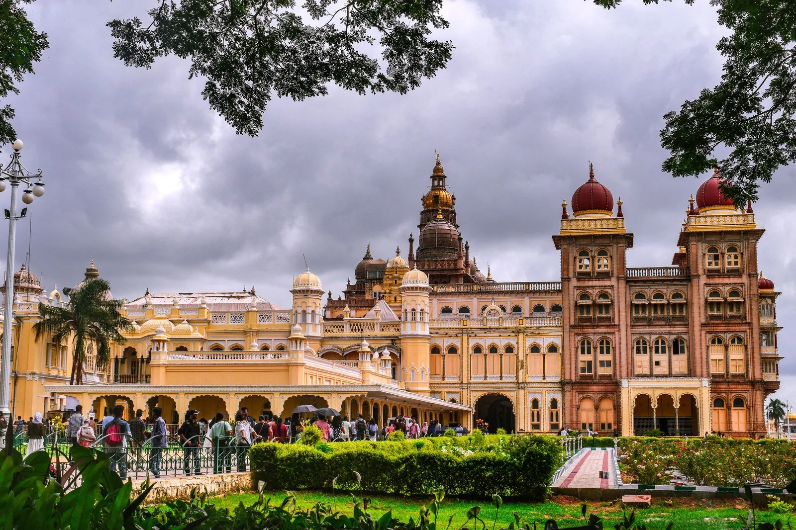 Visitors in the gardens of the Mysore Palace under a monsoon sky