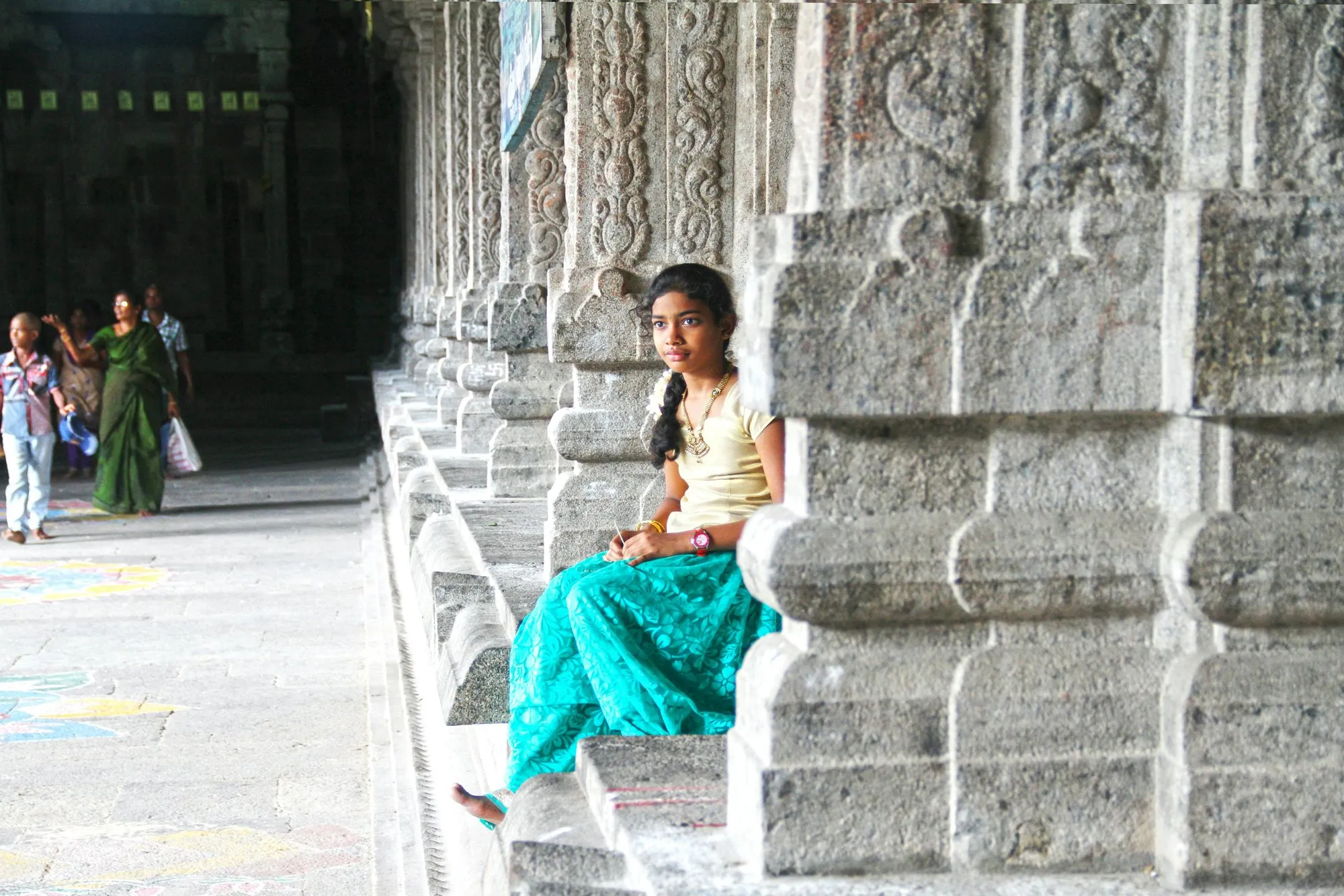 A girl in a teal skirt resting on carved temple steps