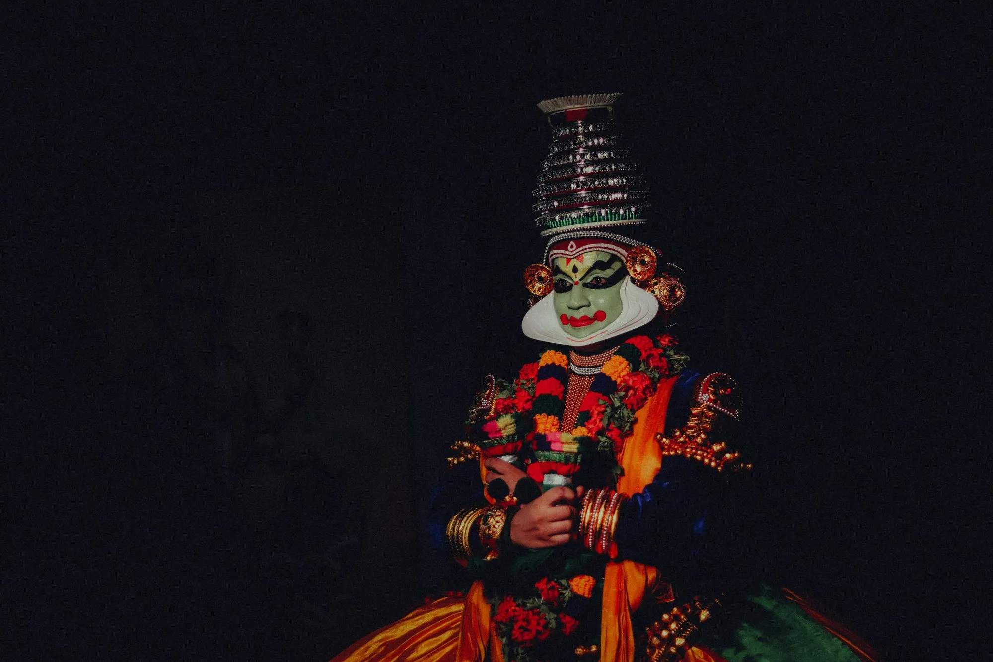 A Kathakali dancer in full make-up and crown against a dark stage