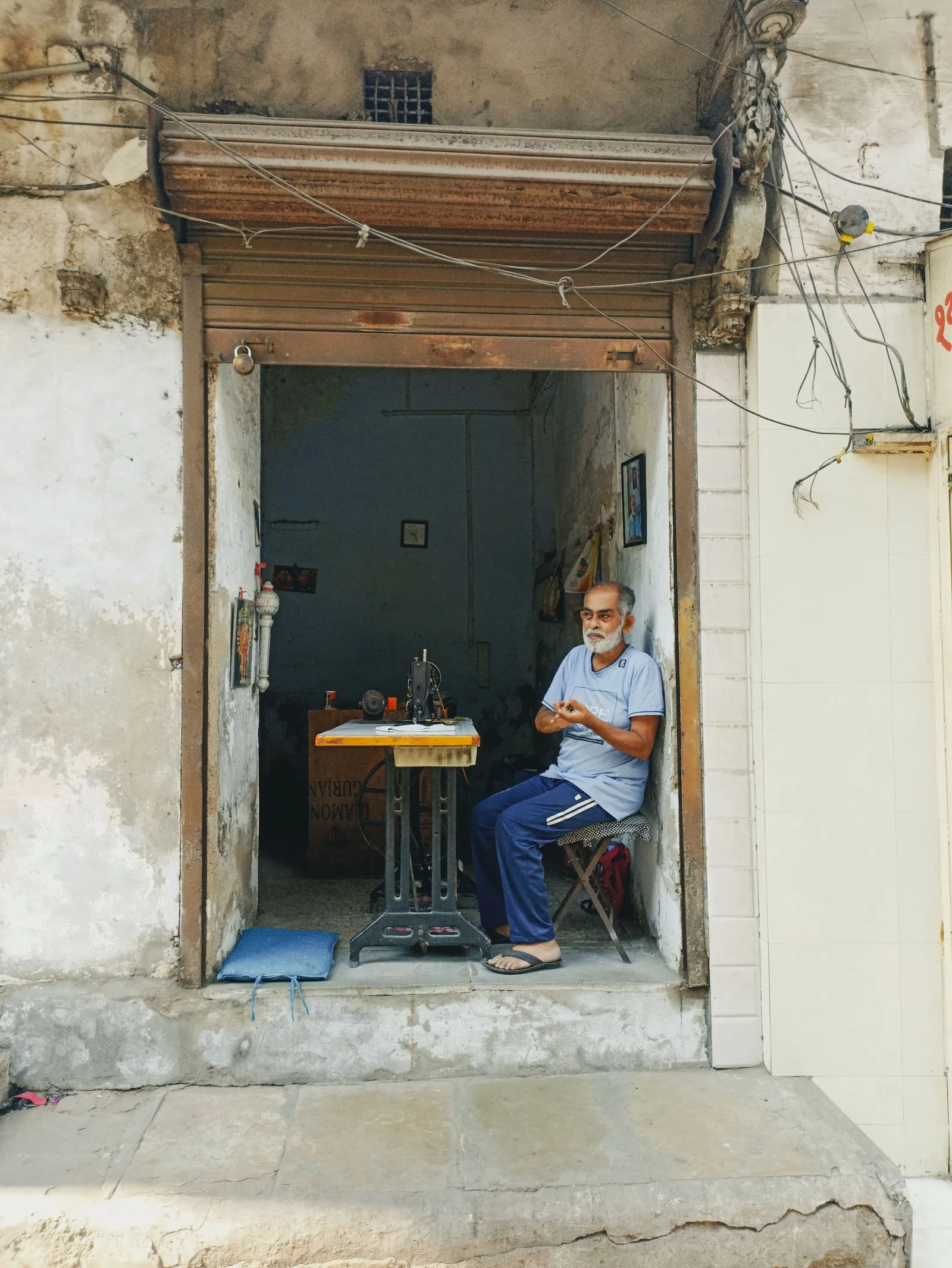 A tailor beside his sewing machine in the doorway of his Ahmedabad workshop