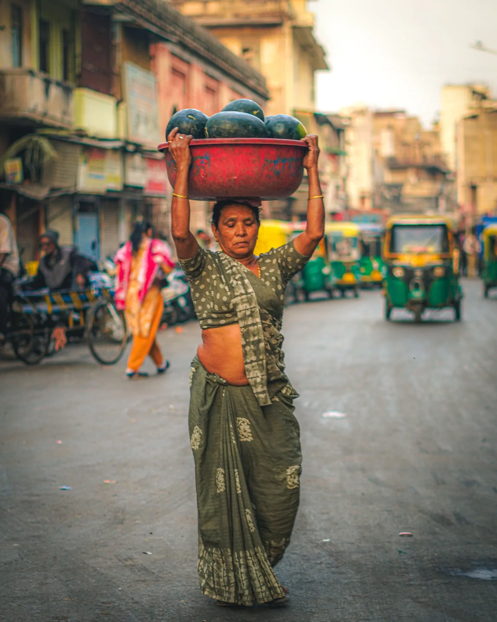 A woman carrying watermelons on her head through an Ahmedabad street