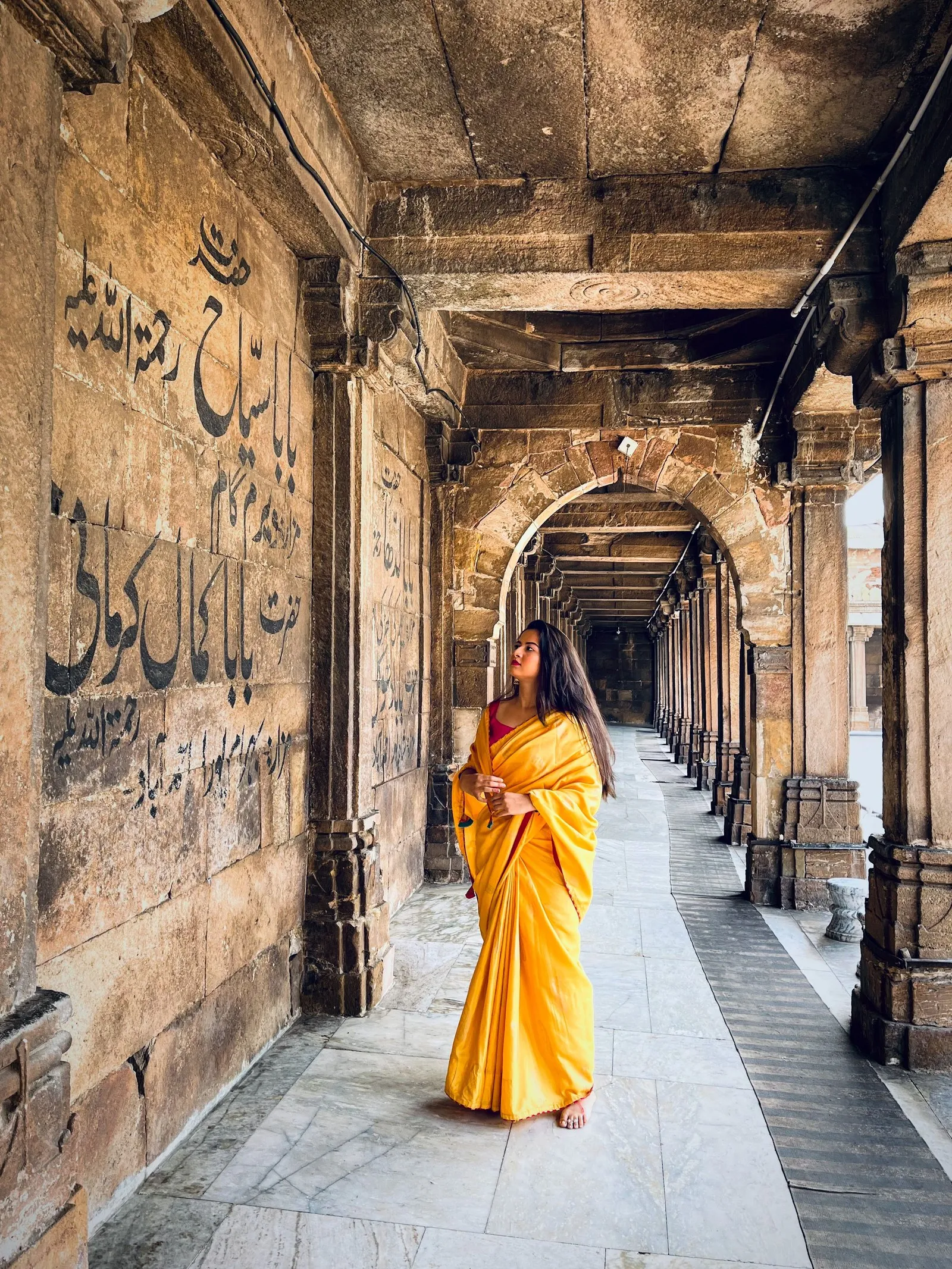 A woman in a yellow sari in the colonnade of the Jama Masjid, Ahmedabad