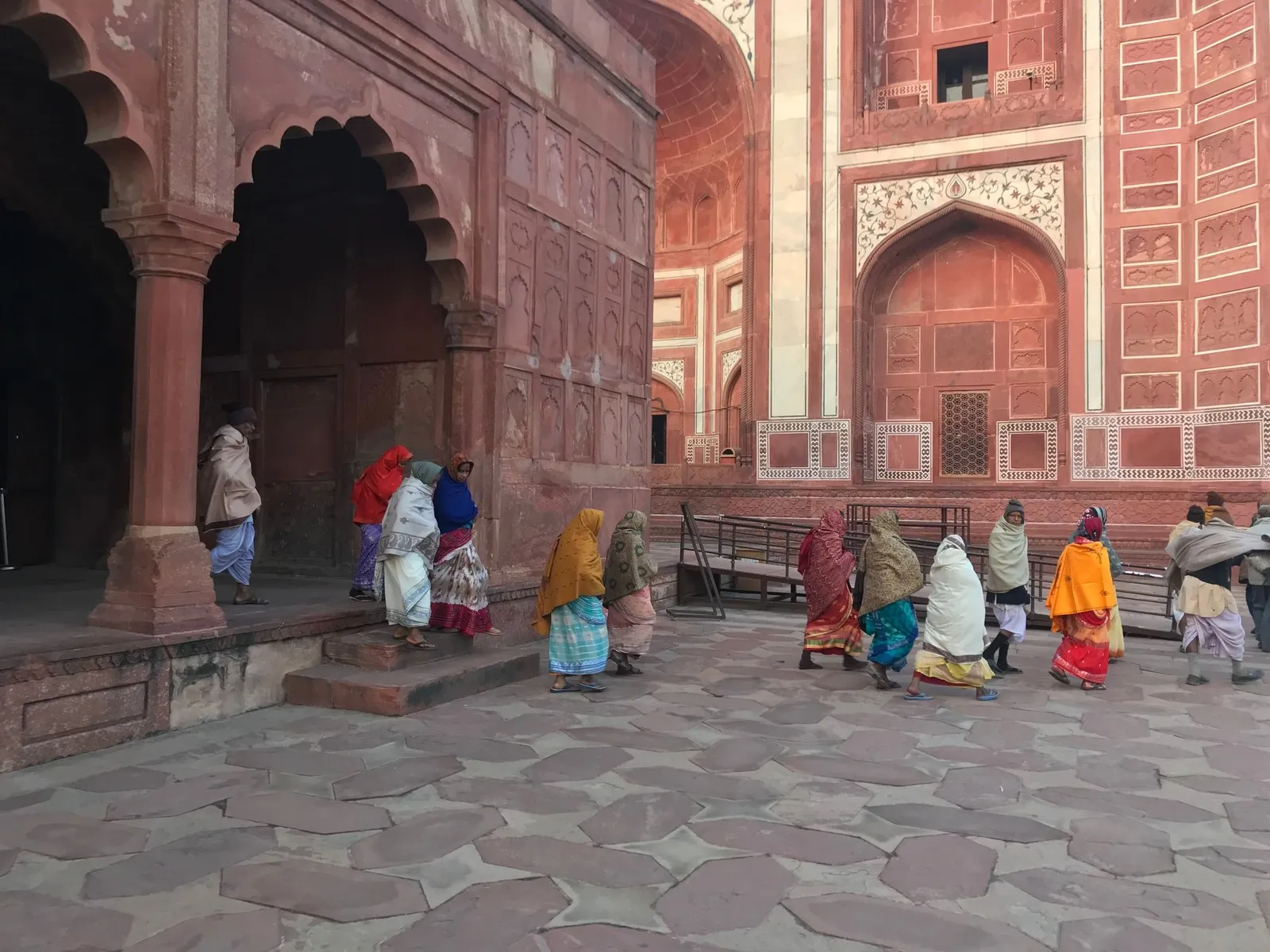 Women in saris resting by red sandstone arches in Agra