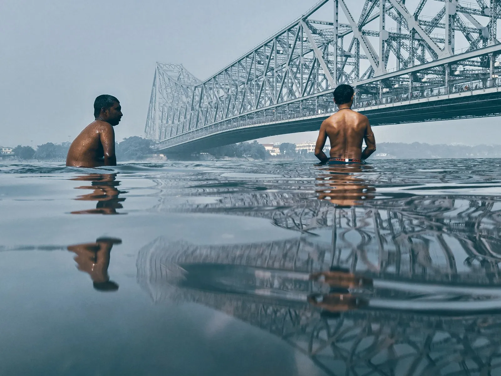 Men bathing in the Hooghly, Howrah Bridge behind them, Kolkata