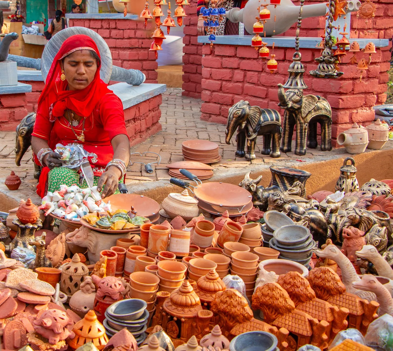 A woman in a red veil selling clay pots and lamps at a Jaipur market