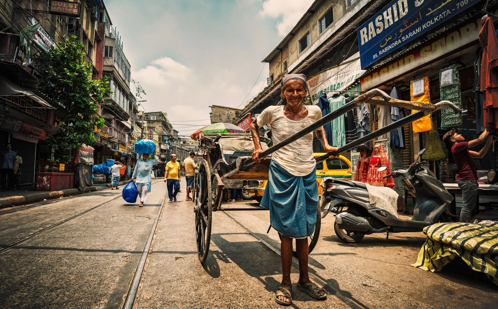 An elderly man pulling a hand-drawn rickshaw along a Kolkata street