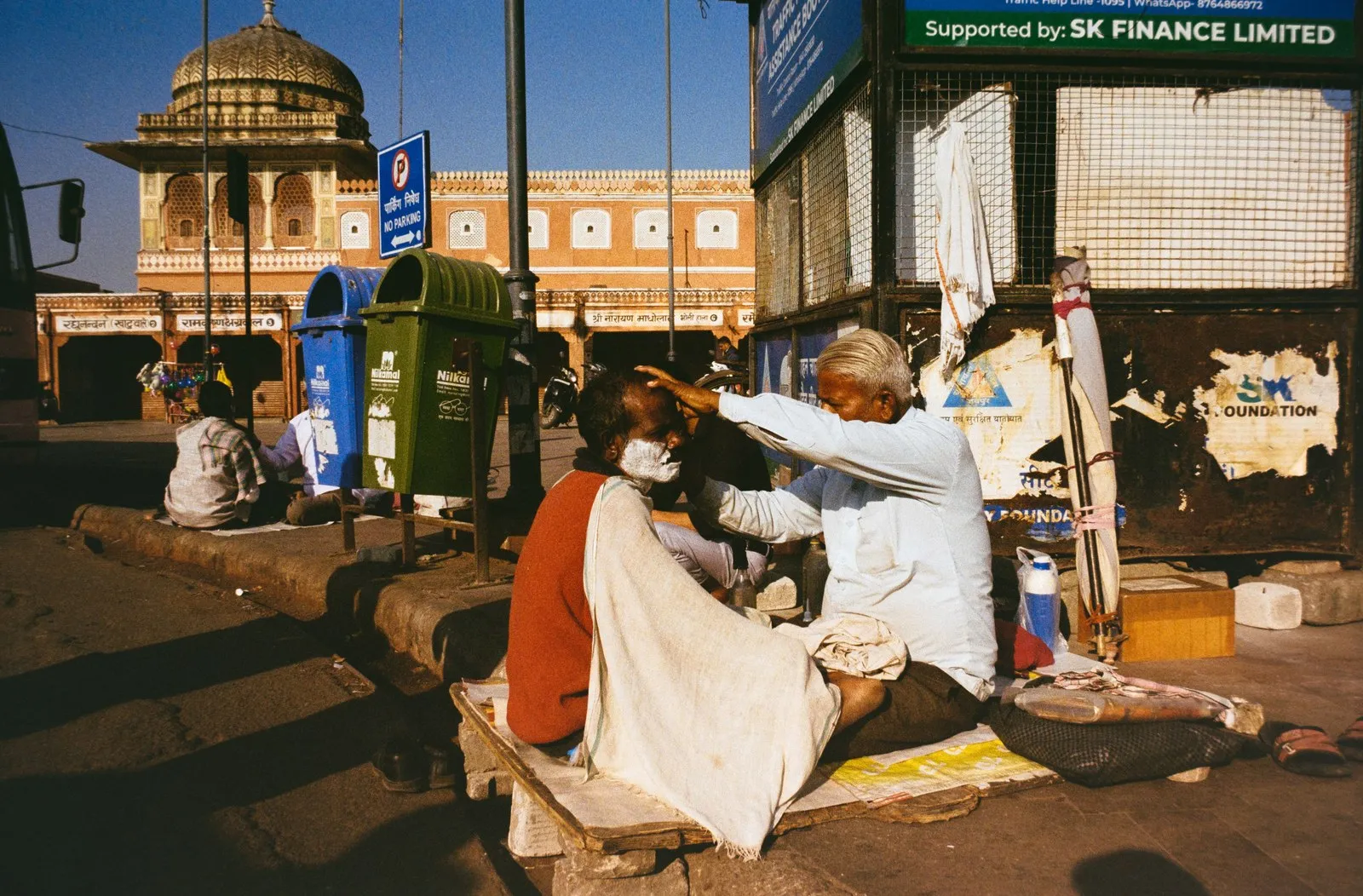 A street barber shaving a customer on the pavement in Jaipur