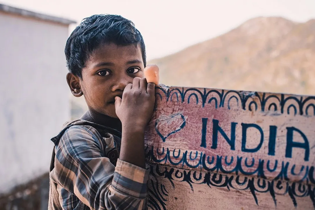 A boy beside a wall painted with the word India