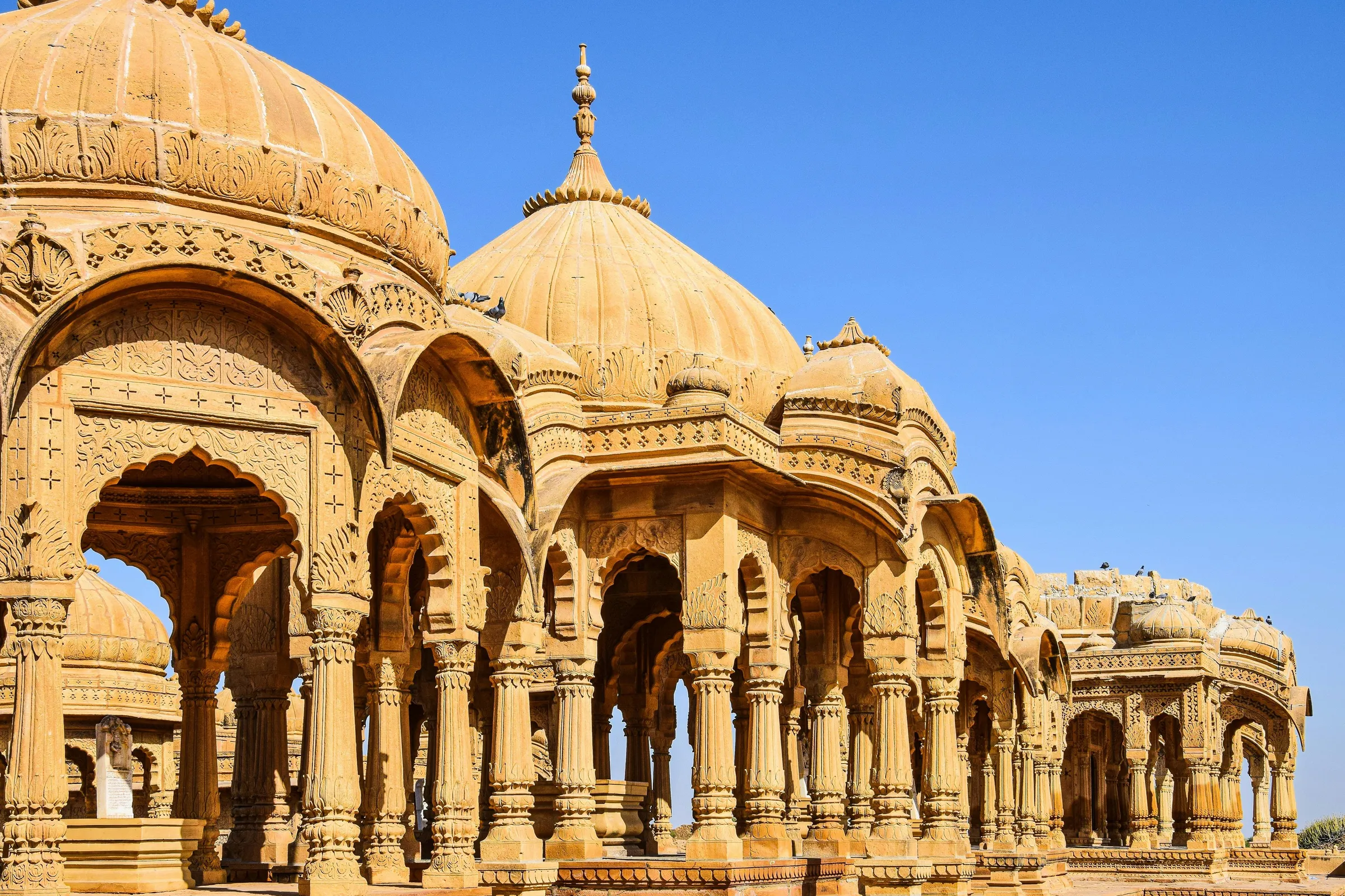 Sandstone cenotaphs with carved domes under a deep blue sky