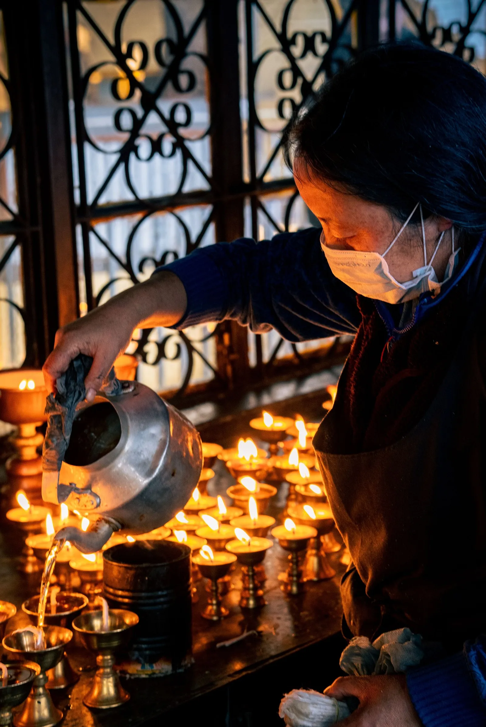 A woman refilling the lamps at a temple in Dharamshala